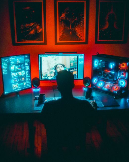 A gamer engrossed in a vibrant RGB computer setup with dual monitors at night.
